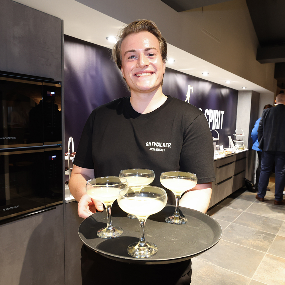 A waiter holding a tray of Outwalker Whiskey cocktails.